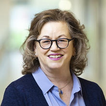 Smiling woman wearing black glasses and blue shirt with cardigan.