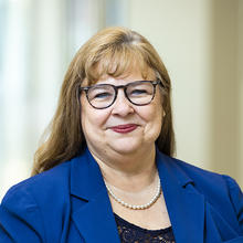 Smiling woman with black glasses wearing a royal blue jacket.