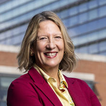 Smiling woman with short, blond hair wearing a red jacket.