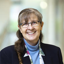 Smiling woman with long hair and glasses wearing a blue shirt.