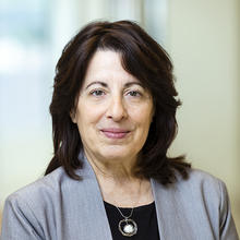 Smiling woman with dark brown hair wearing black shirt and gray jacket.