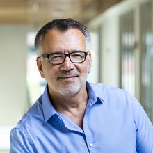 Smiling man wearing black glasses and a blue dress shirt.