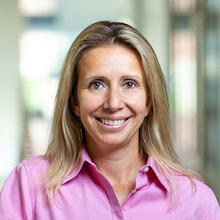 Smiling woman with long, blonde hair wearing a light pink dress shirt.