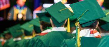 Students sit in rows wearing green caps and gowns for graduation at Mason's Patriot Center.